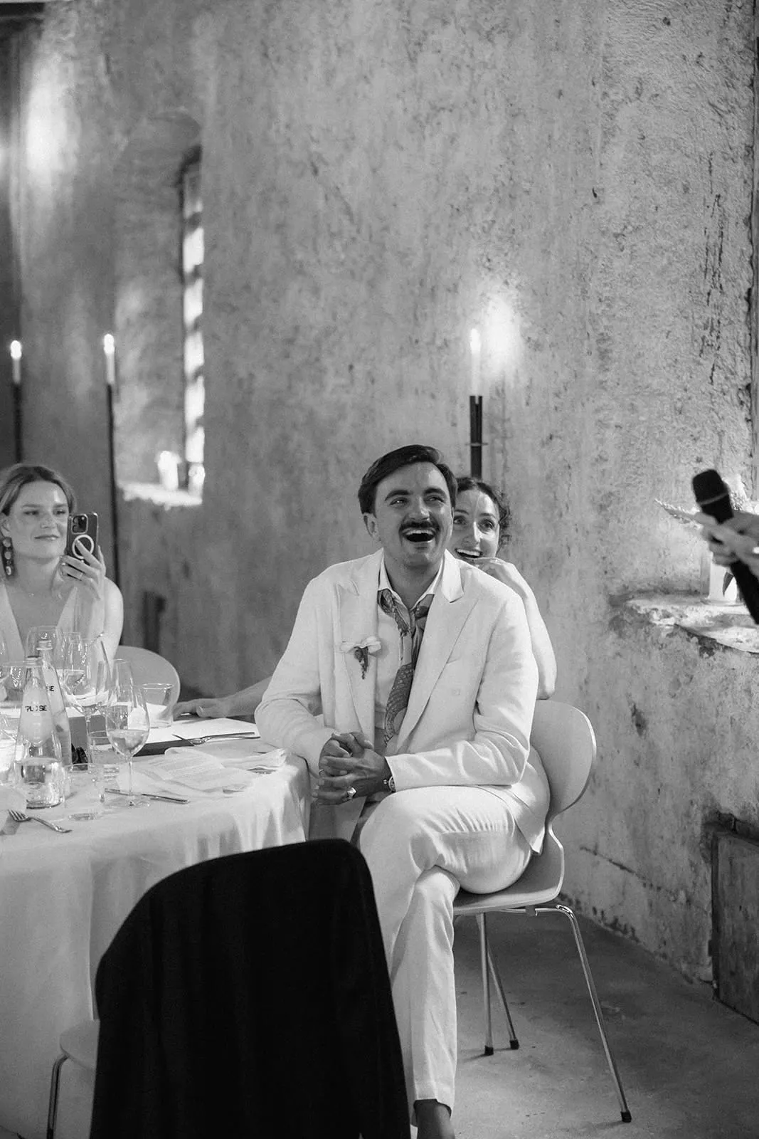 The groom laughing through a speech, a guest filming beside him