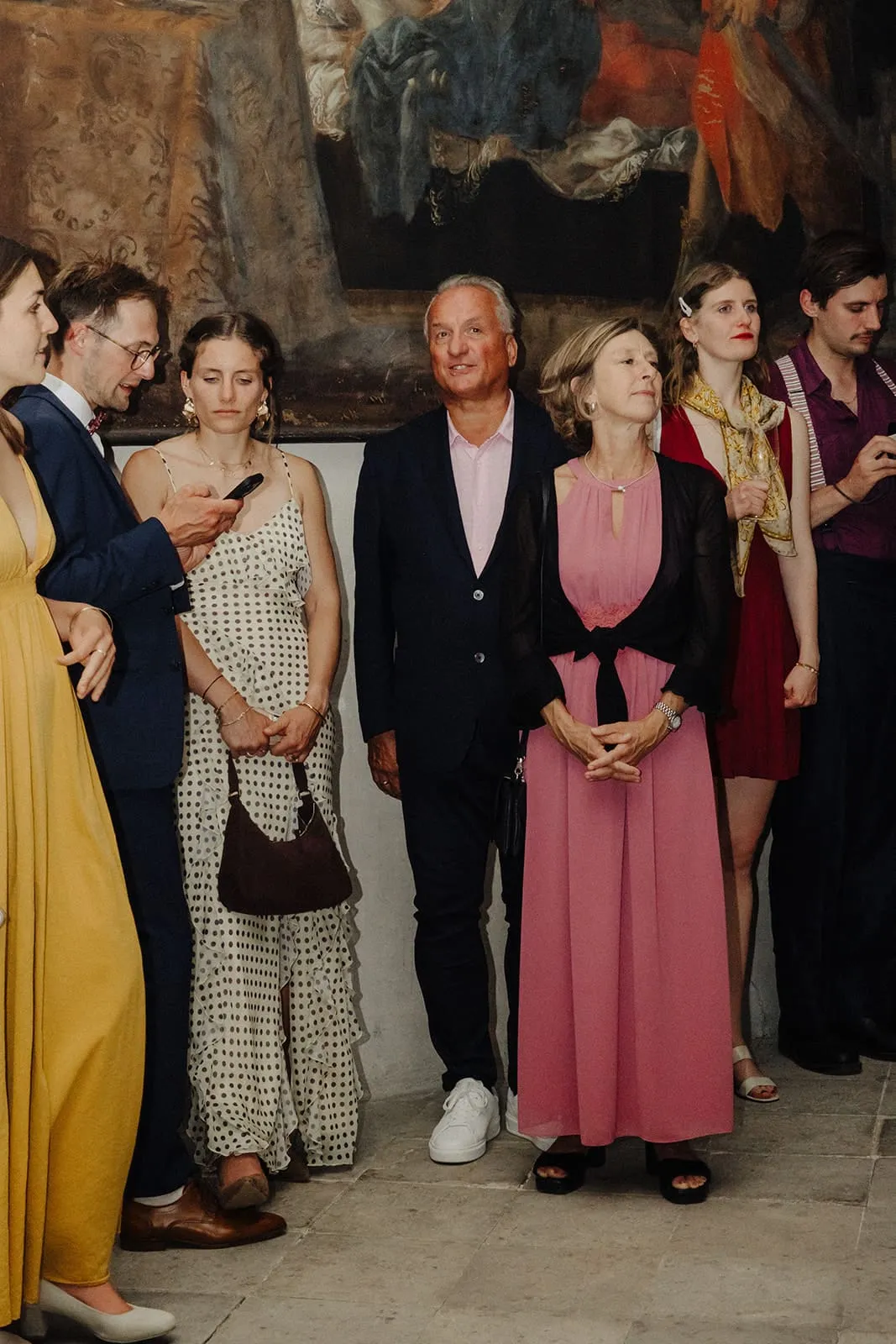 Guests standing in a row under a large old painting, waiting