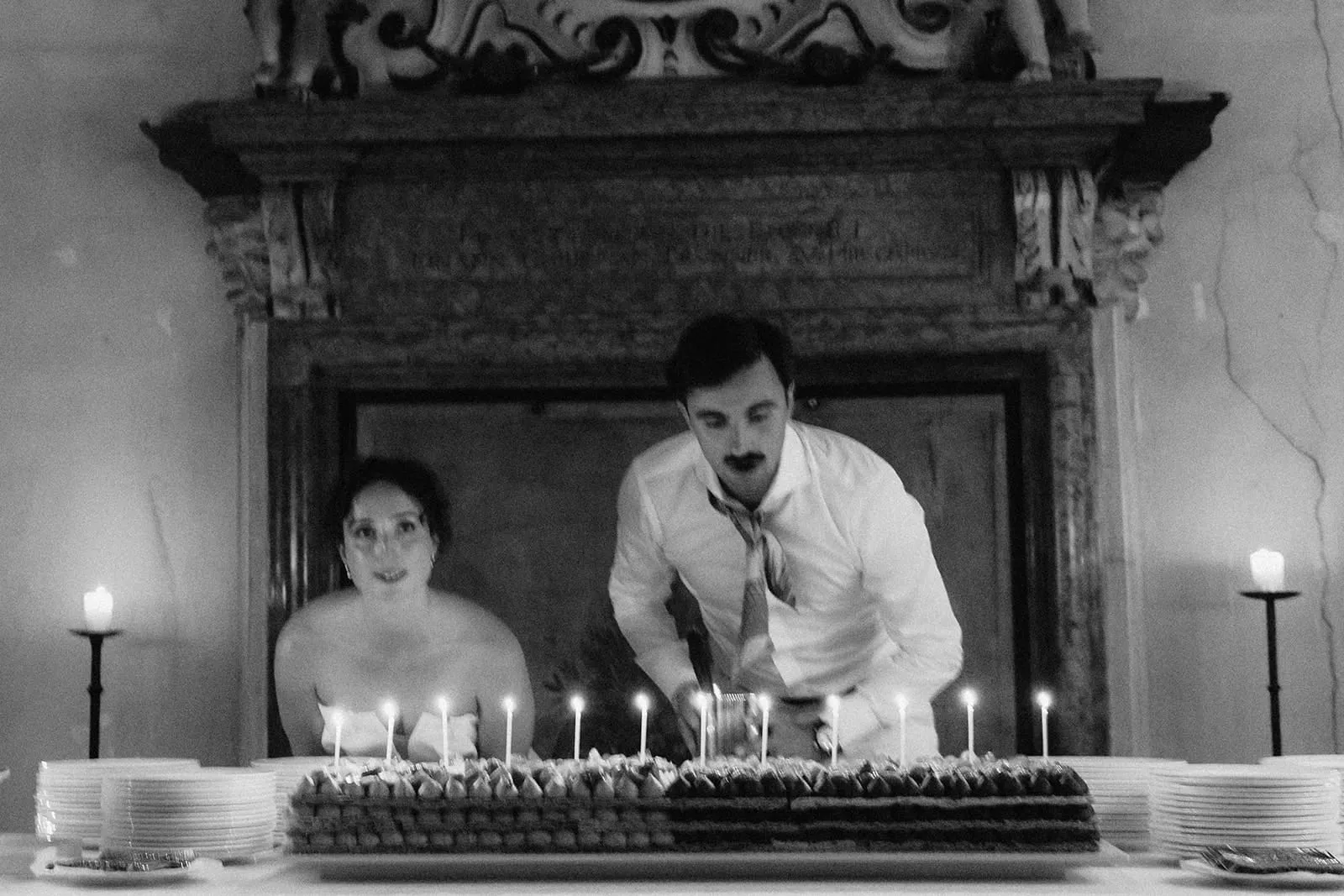 The couple leaning over the candlelit cake in front of the fireplace