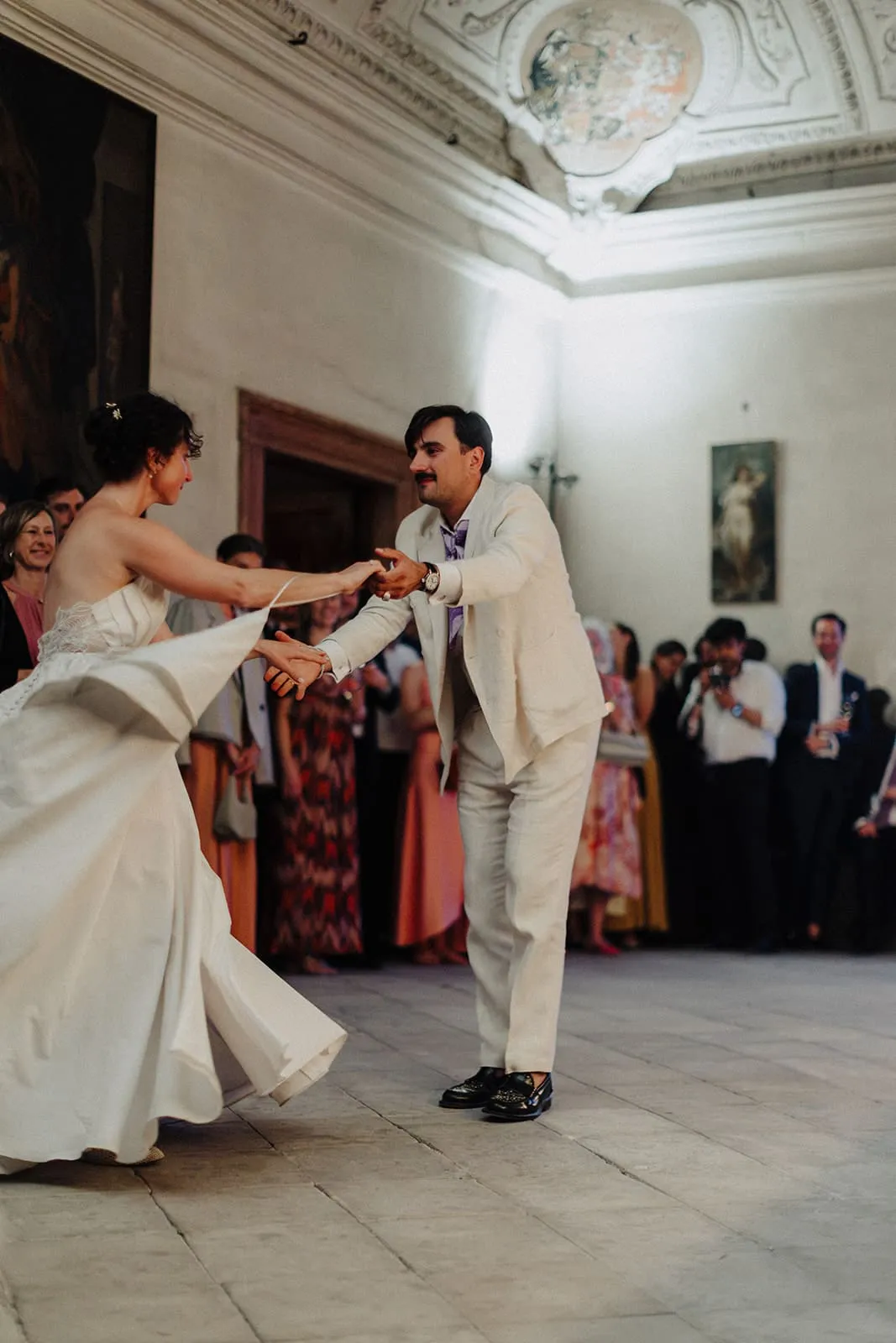 The couple dancing, her skirt swinging out, guests along the wall