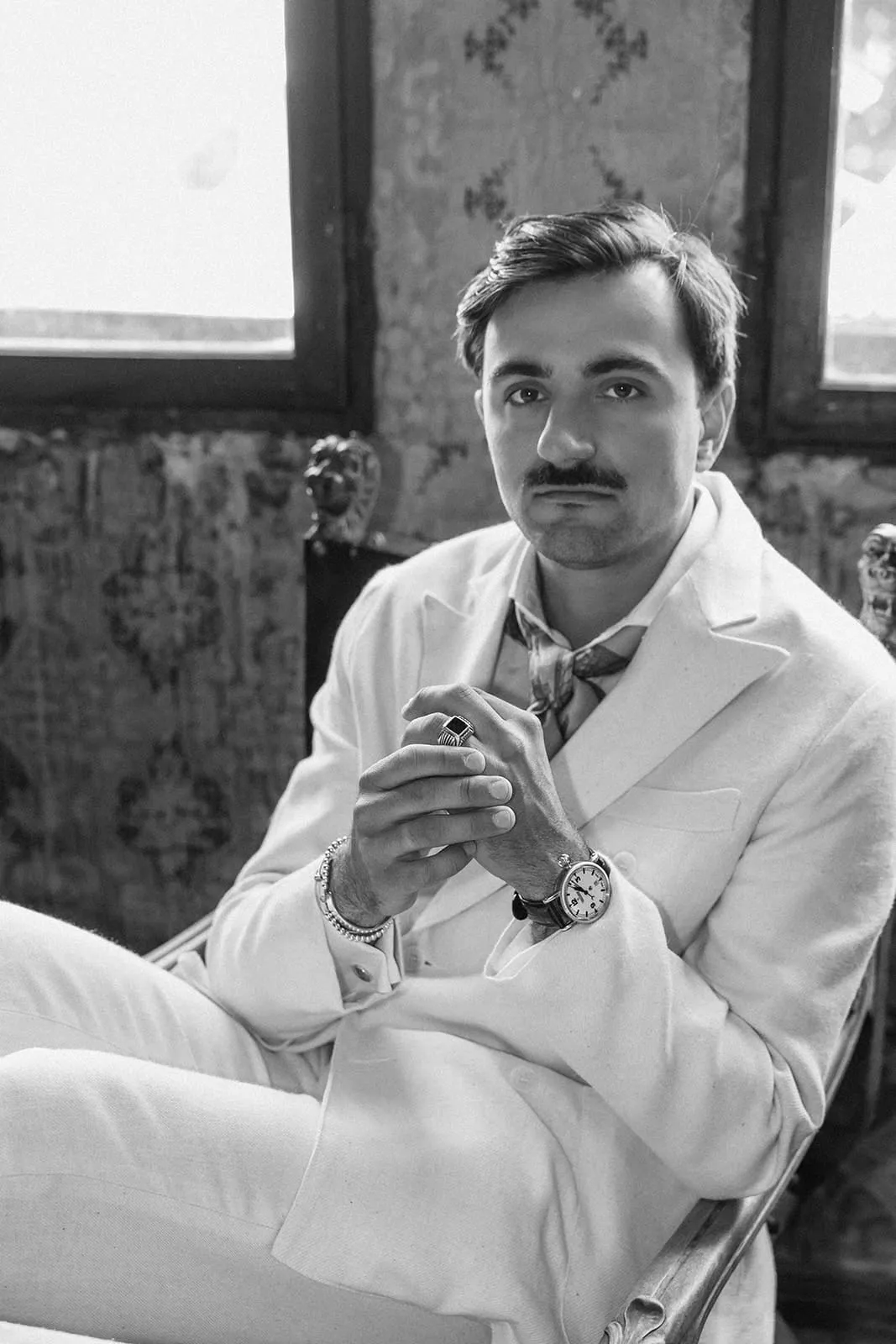 The groom in his cream suit in an armchair, looking into the camera