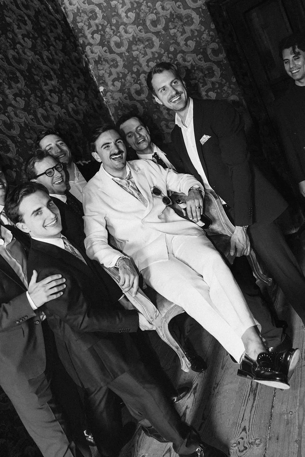 The friends carrying the groom on his chair, everyone laughing