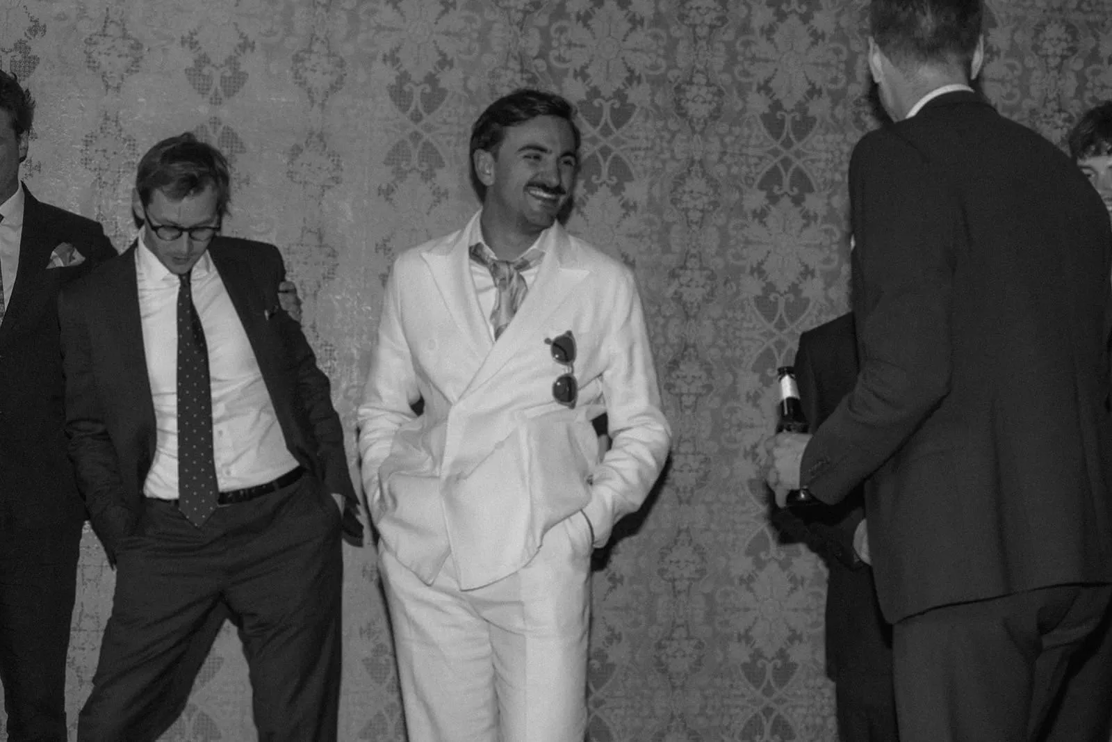The groom laughing among his friends against the papered wall