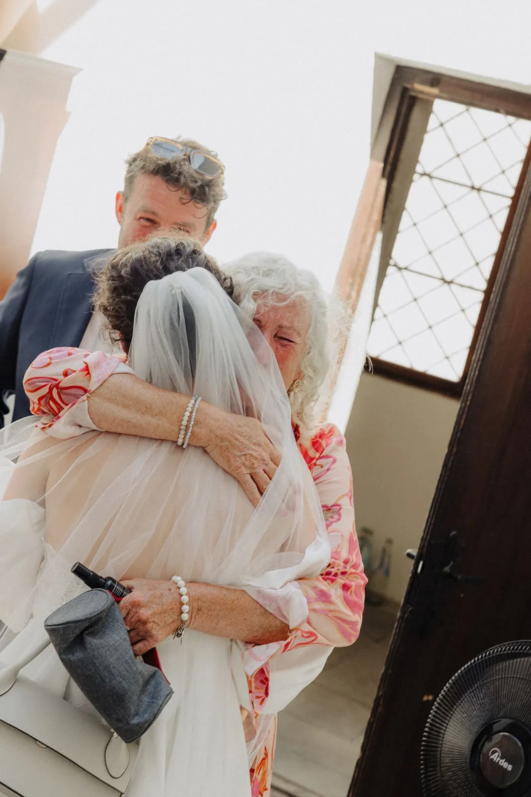 The bride and an older guest holding each other in the doorway, both in tears