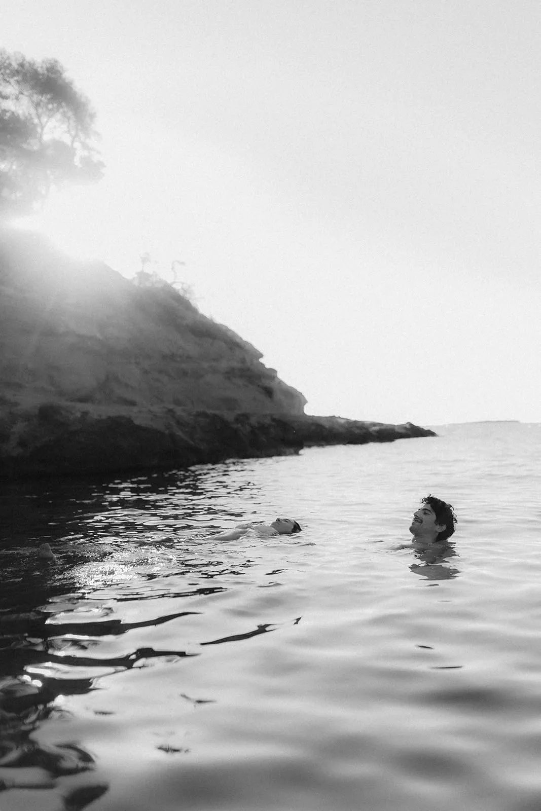 The couple swimming towards the rocks, the sun rising over the headland