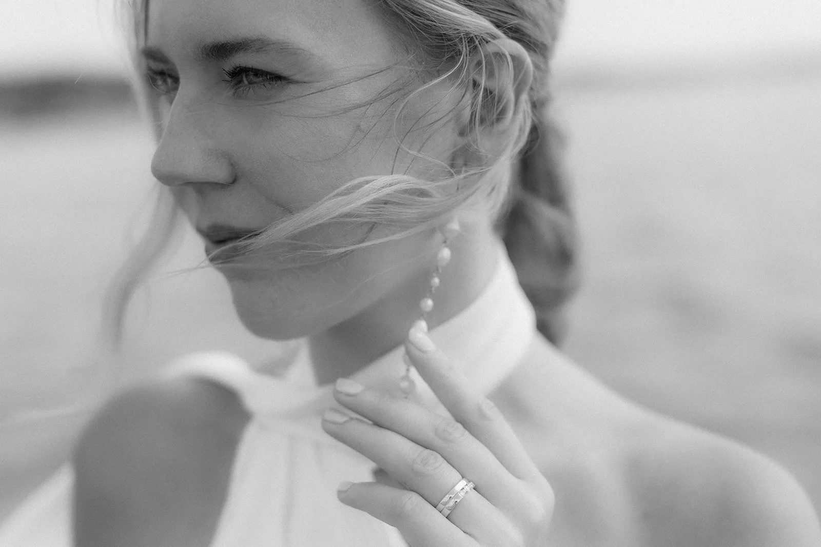 A bride in profile, veil across her face, hand at her collar