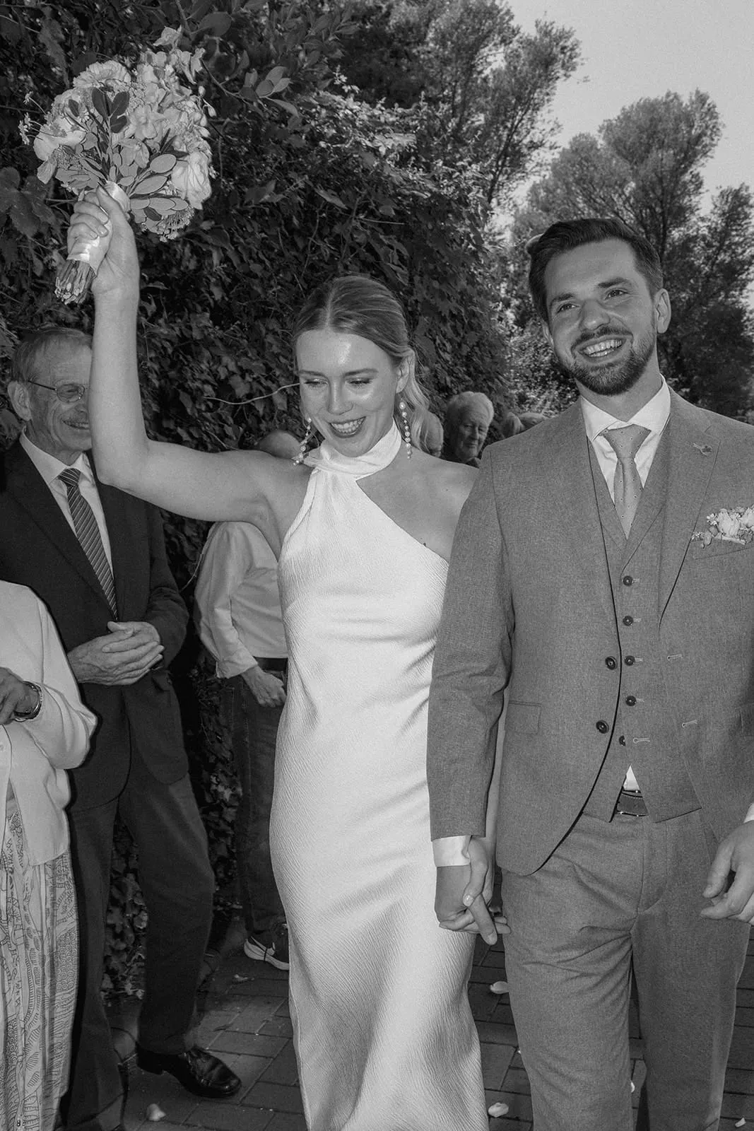 The bride lifting her bouquet over her head, the groom laughing beside her