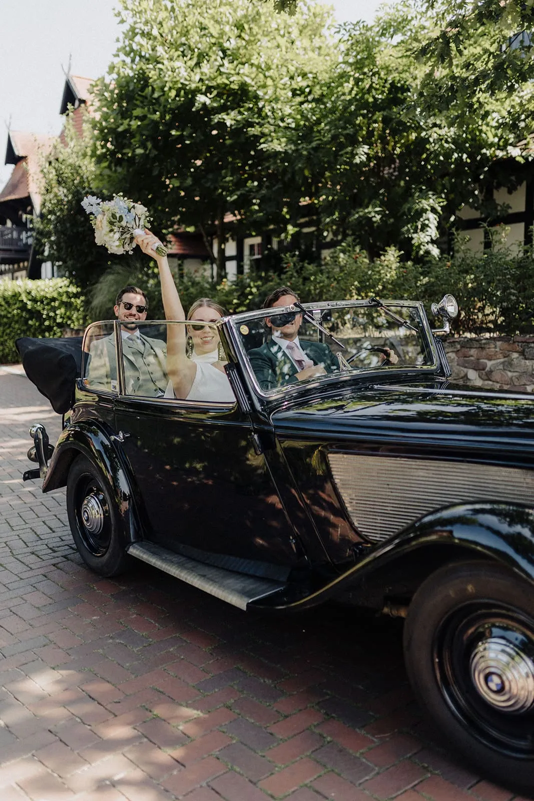 The bride raising her bouquet from the back seat of the open car