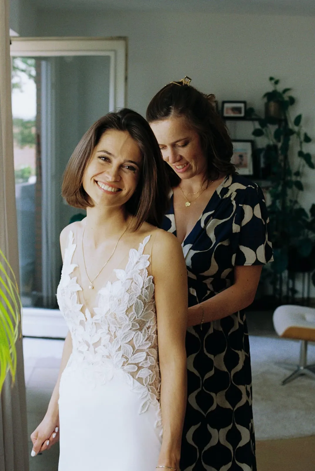 A friend doing up the lace dress, the bride laughing over her shoulder